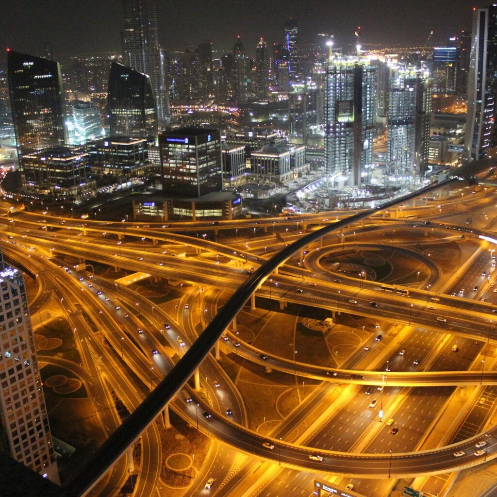Overhead shot of Dubai at night showcasing glowing highways interwoven like a network, surrounded by towering skyscrapers and bustling city lights, symbolizing opportunities for business growth with leading business setup consultants in Dubai, UAE